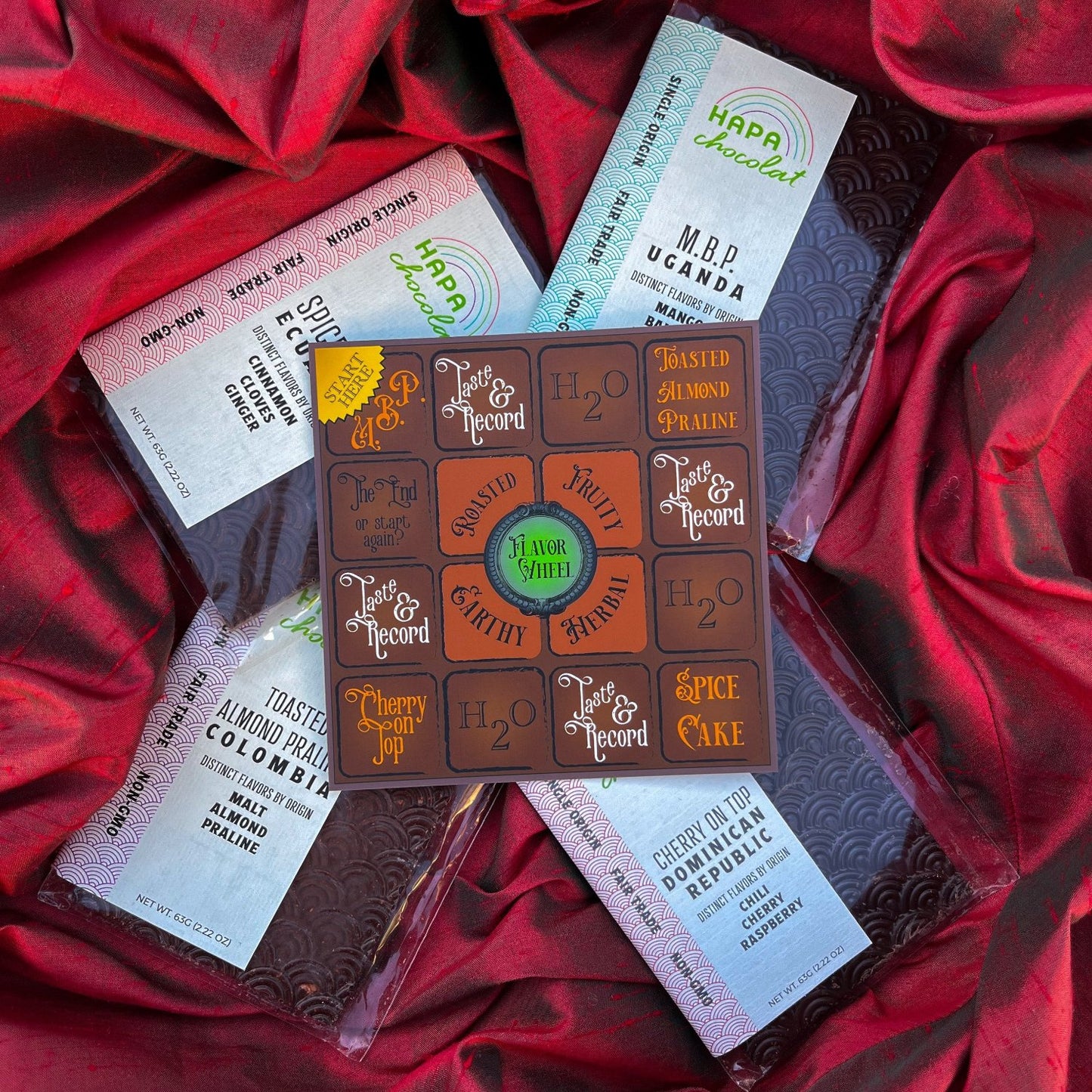 A chocolate brown game board is on top of four Hapa Chocolat bars. All are resting on top of red silk fabric.
