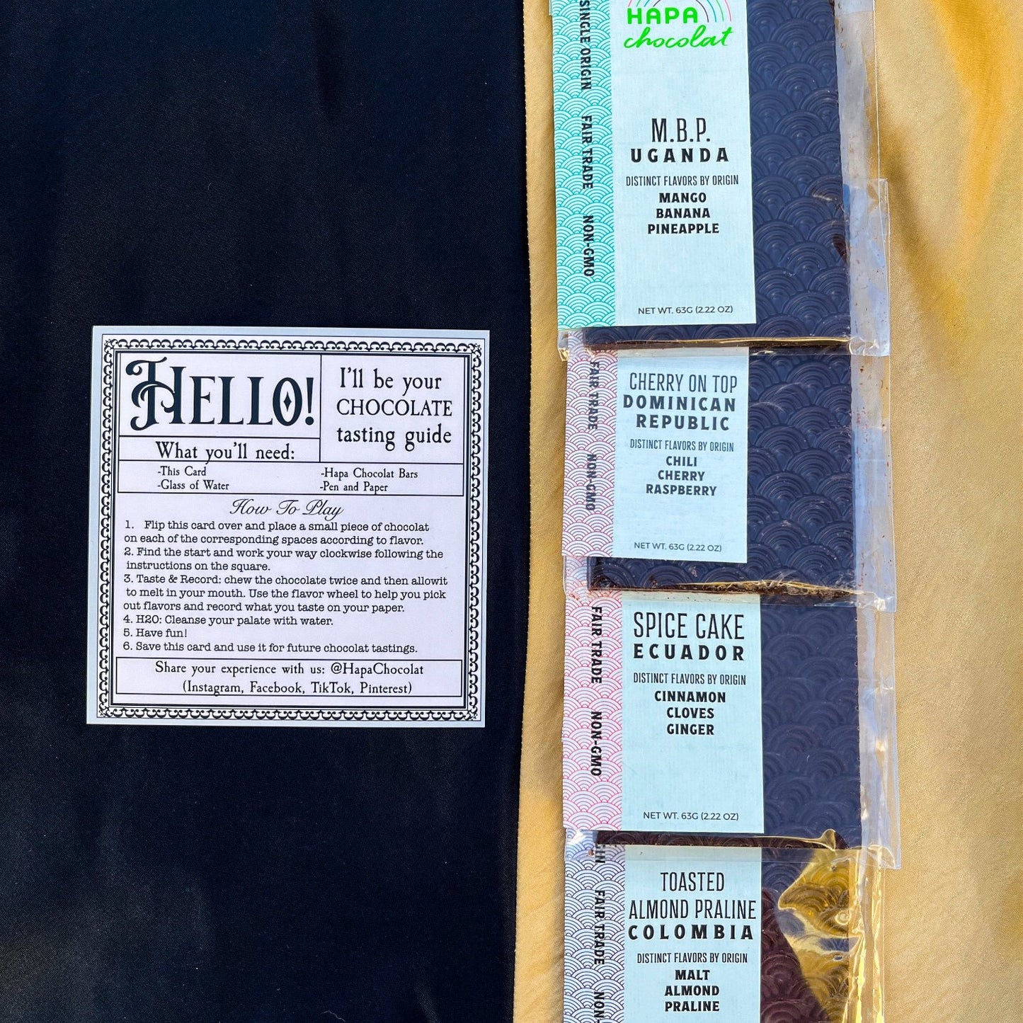On to a black background is a beige card with instructions printed on it. The other half of the image is on a golden yellow background and it is all four Hapa Chocolat bars.