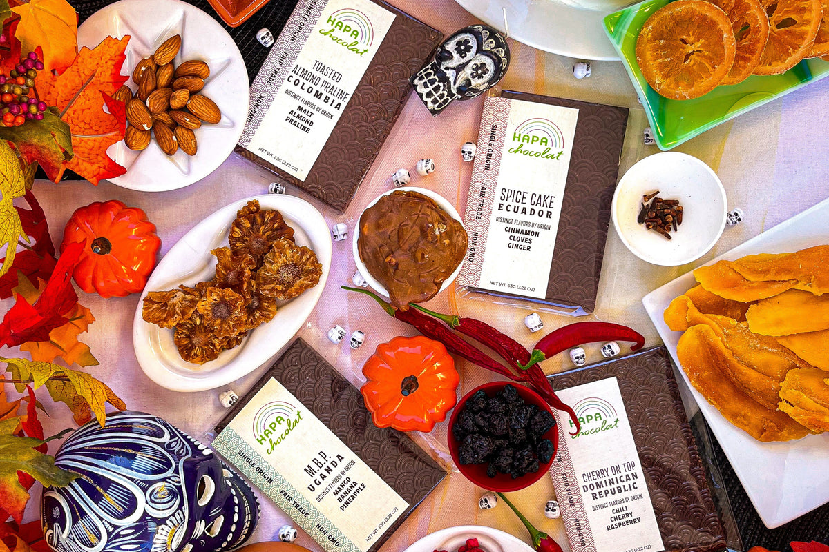 Four Hapa Chocolat bars are placed amongst skull beads and autumn leaves. And surrounded by dried fruits.
