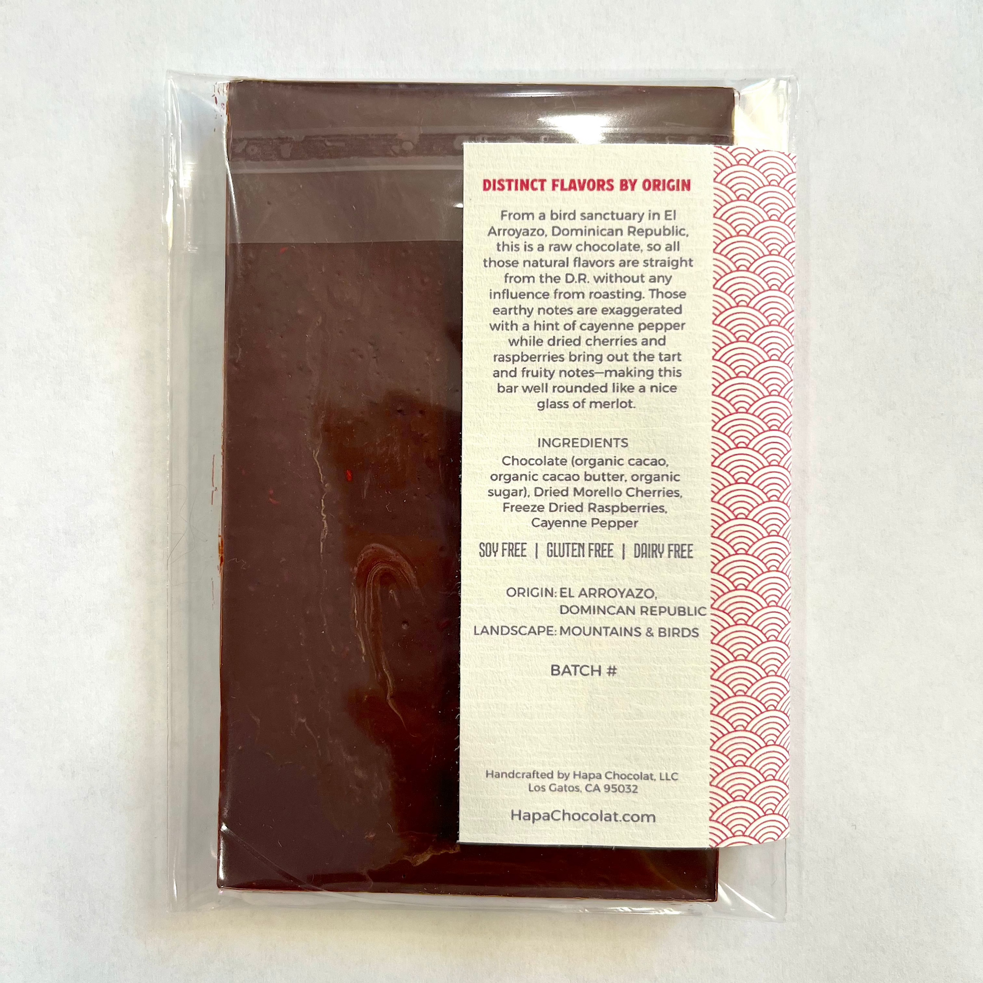 A dark chocolate bar in clear cello packaging with a paper label showing the back information. On a white background.