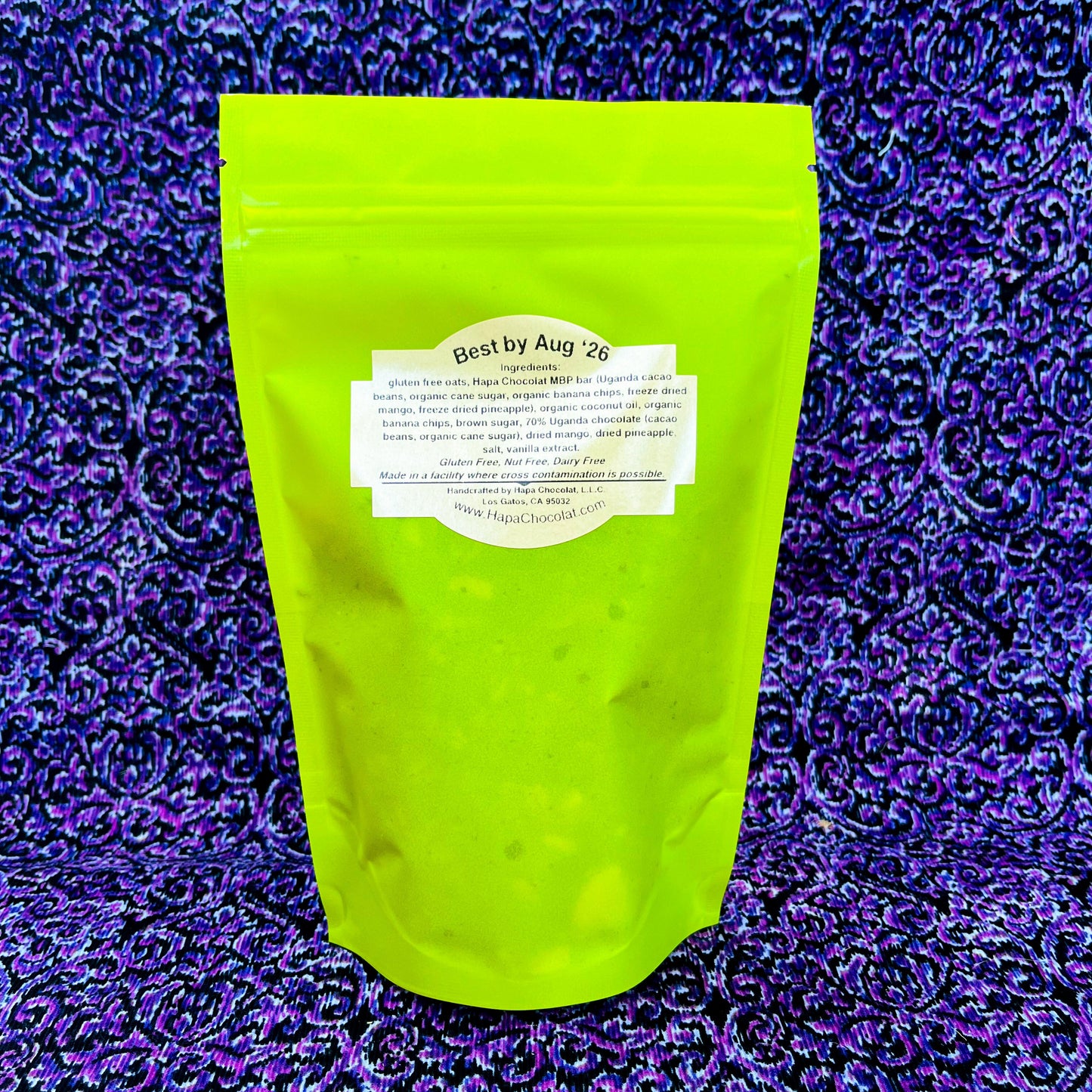 The ingredients label and backside of a bright green full of chocolate covered granola. In front of a purple and black swirled background. 