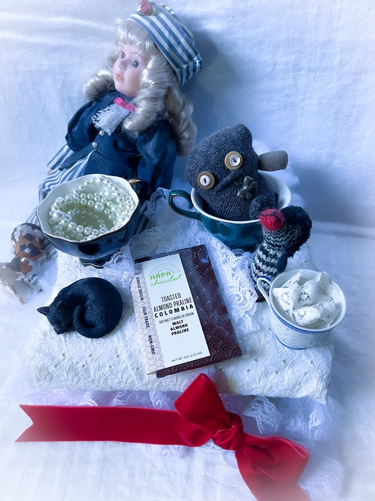 Toys and a doll having a tea party with a dark chocolate bar and lots of lae.