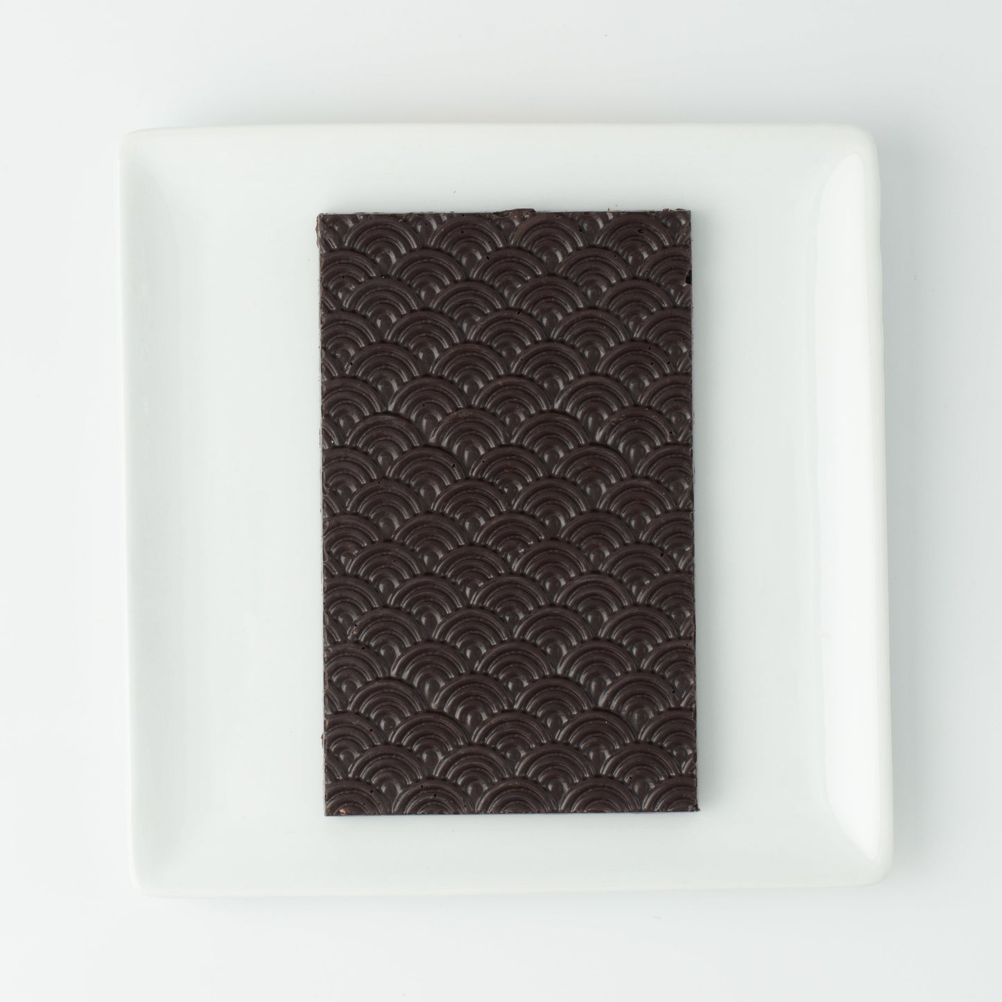 The seigaiha pattern dark chocolate bar on a white square plate, with no packaging.