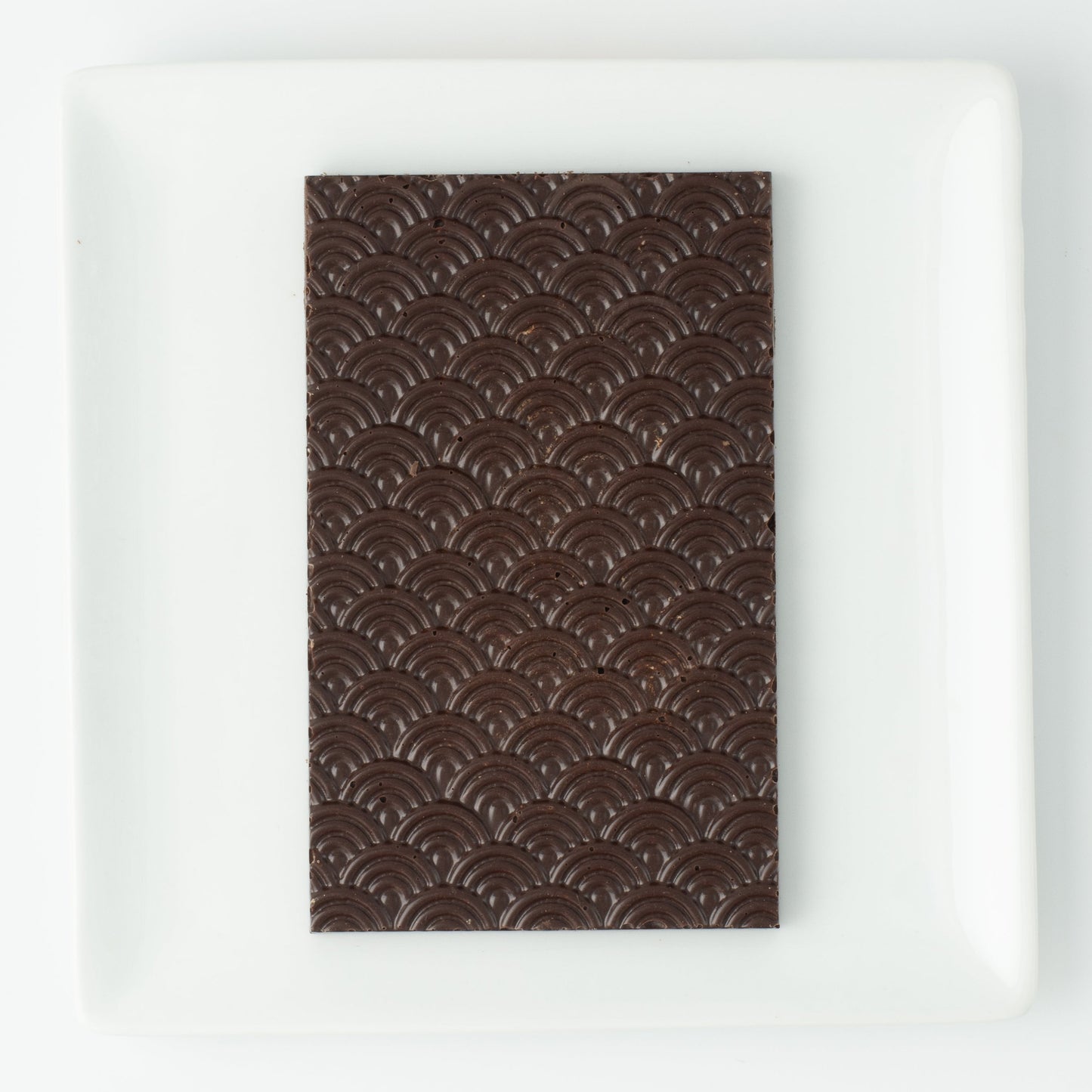 The seigaiha pattern dark chocolate bar on a white square plate, with no packaging.