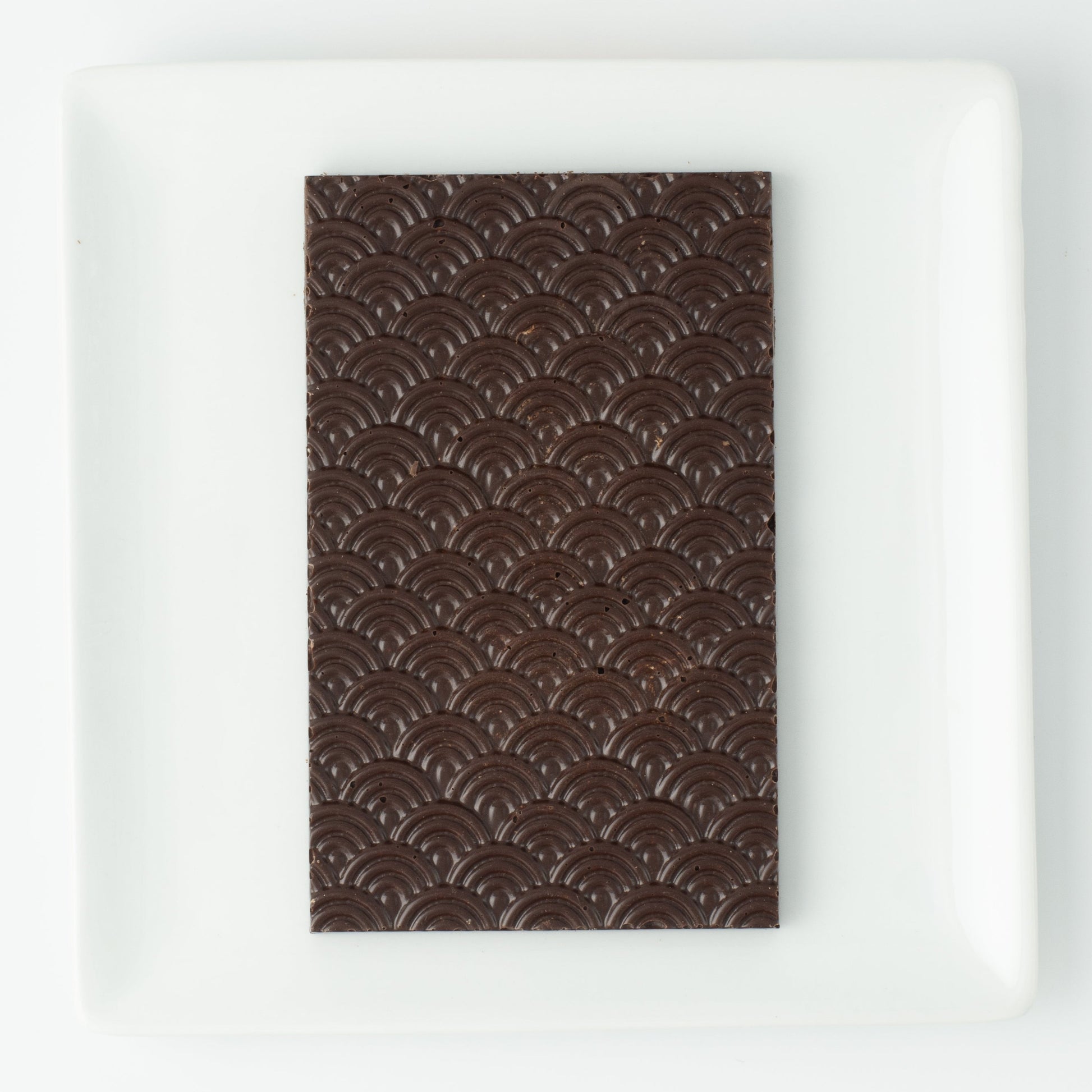 The seigaiha pattern dark chocolate bar on a white square plate, with no packaging.