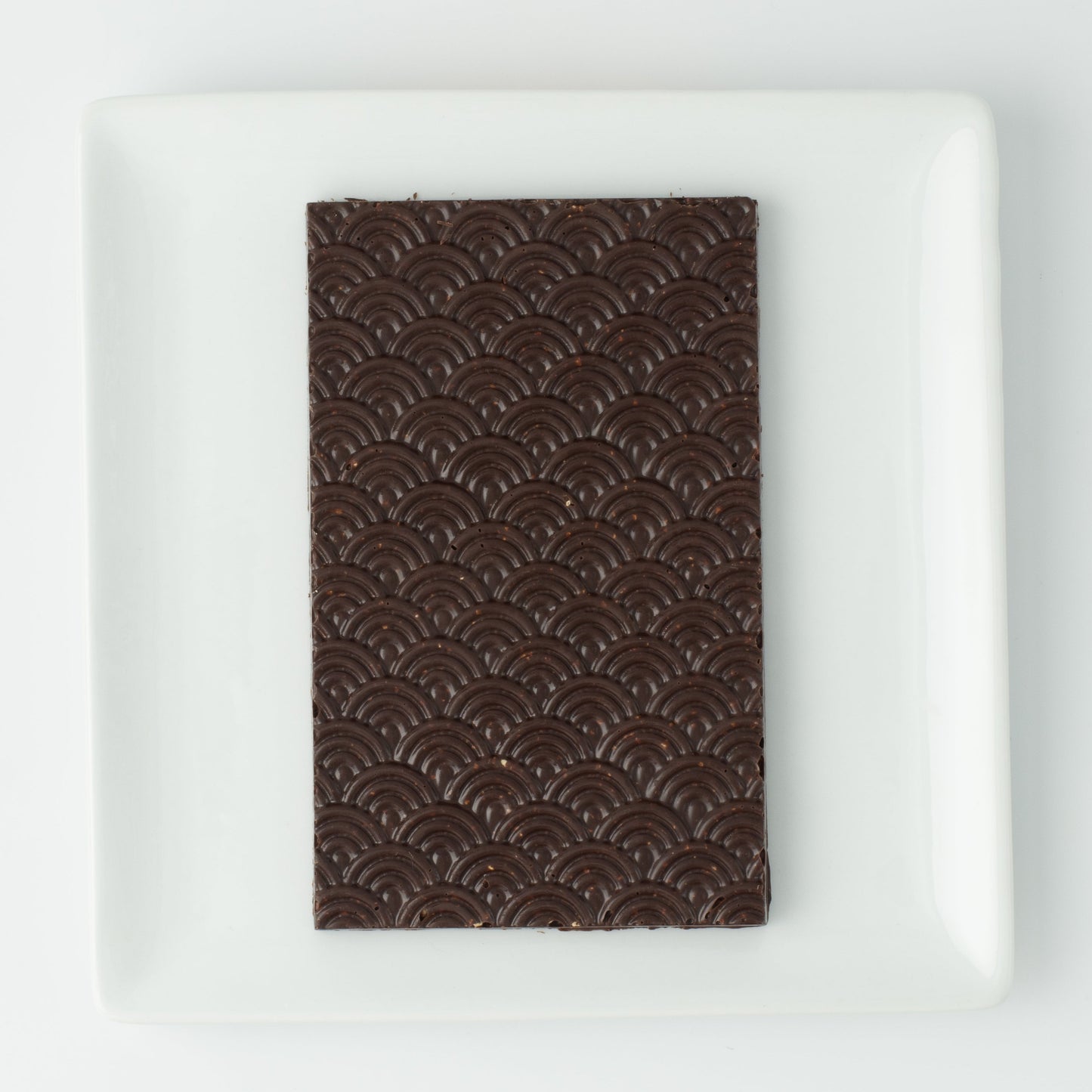 The seigaiha pattern dark chocolate bar on a white square plate, with no packaging.