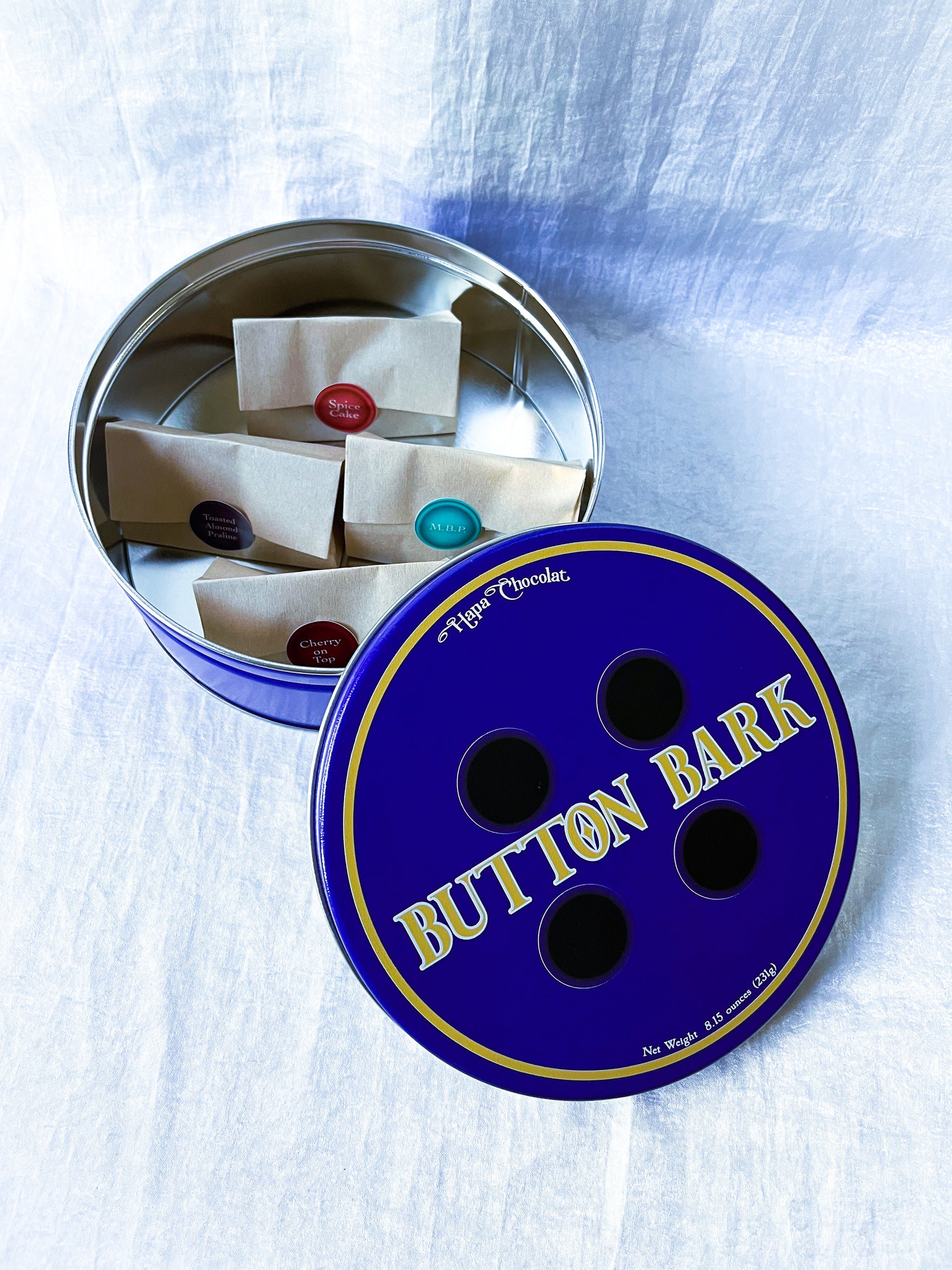 A blue tin full of little brown bags with different colored stickers.