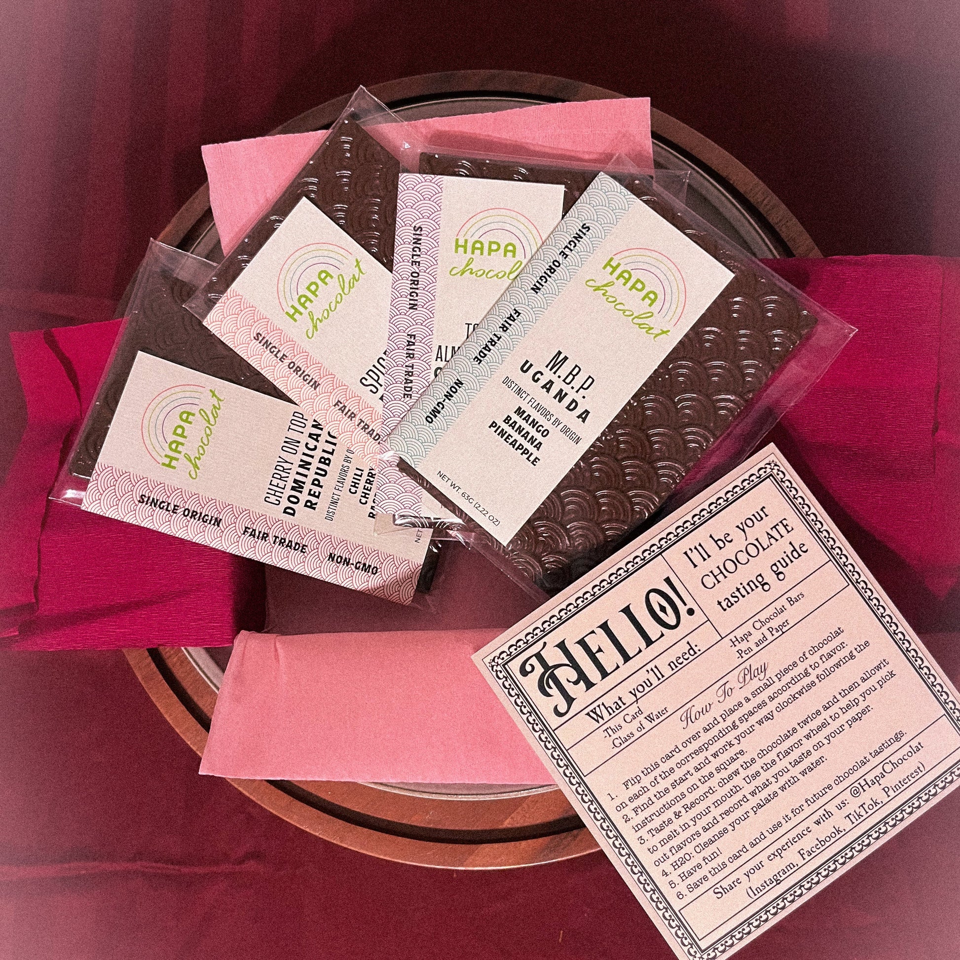 Four dark chocolate bars sit in a pink paper lined box with an instruction guide, on a striped maroon background.