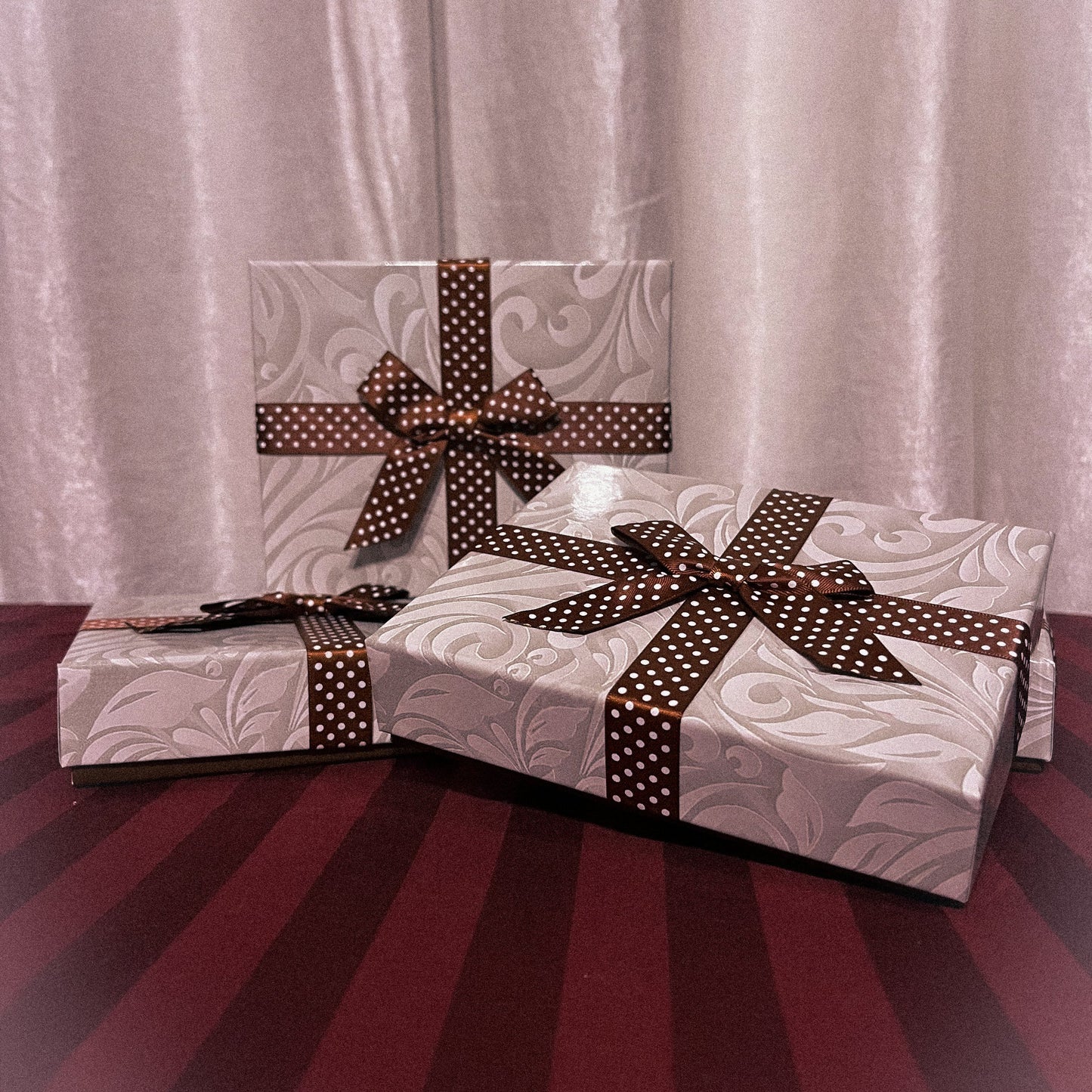 Three ribbon wrapped white gift boxes sit atop a striped maroon table cloth with a shiny white background.